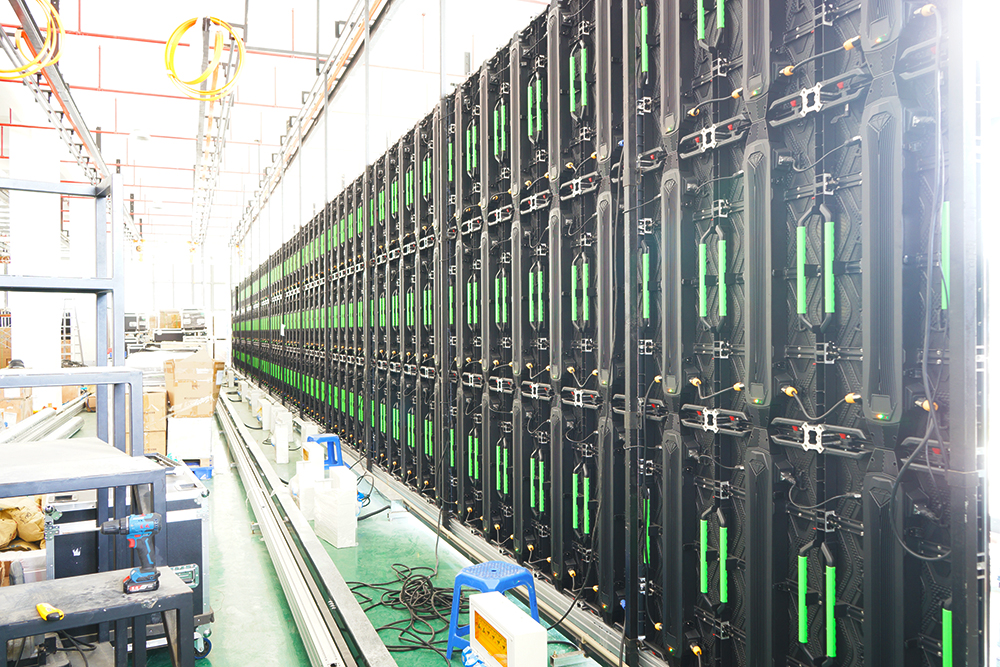 Long row of rear-facing LED cabinets with green handles inside a workshop.