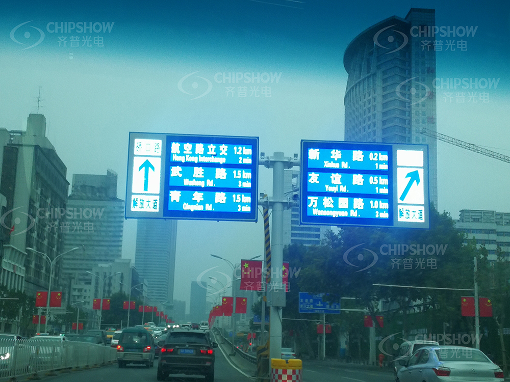 Blue overhead electronic direction signs with arrows above a city street.