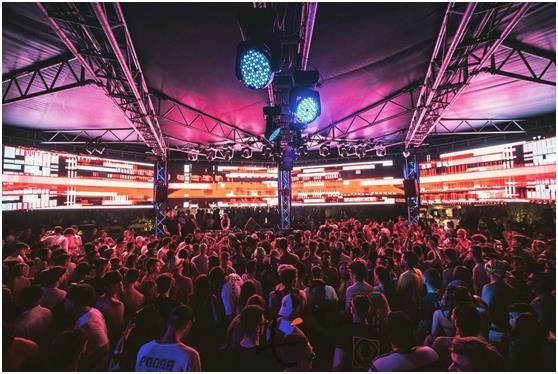 Wide screens showing red graphics above a crowd under an illuminated canopy.