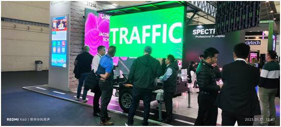 Visitors gathered at an exhibition booth in front of a bright green screen.