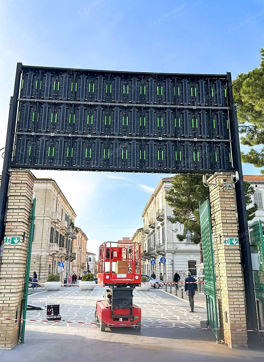 Rear of an overhead LED screen above an entrance, with a scissor lift below.