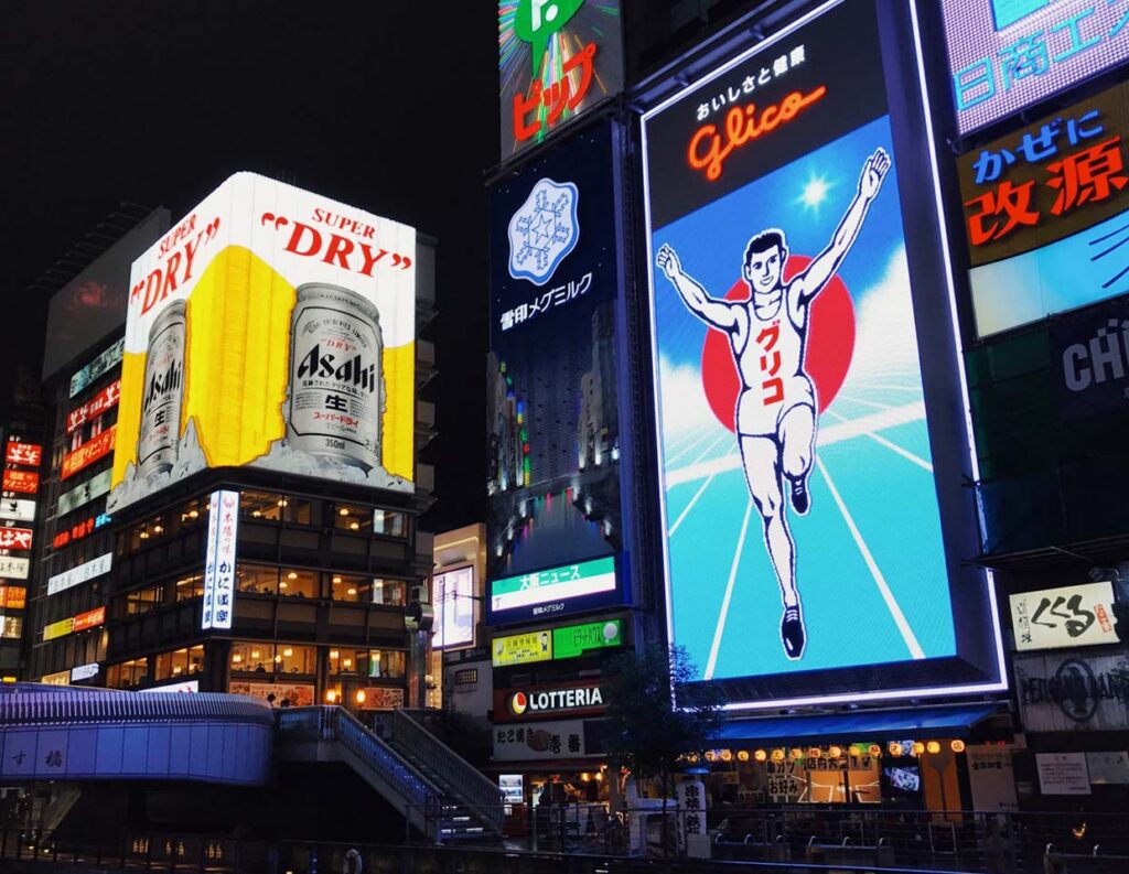 Nighttime cityscape with multiple bright LED billboards showing colorful ads on buildings in a busy commercial area