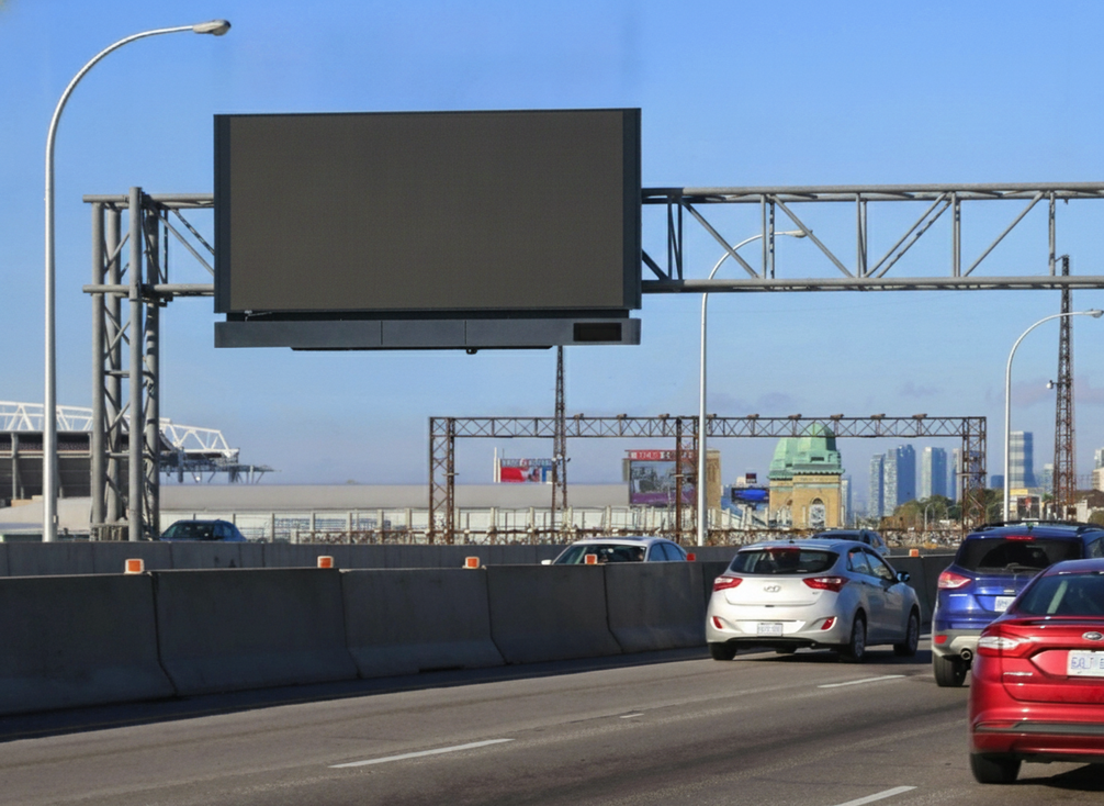 A gantry-mounted variable message sign spans a high-speed highway corridor with traffic moving below.