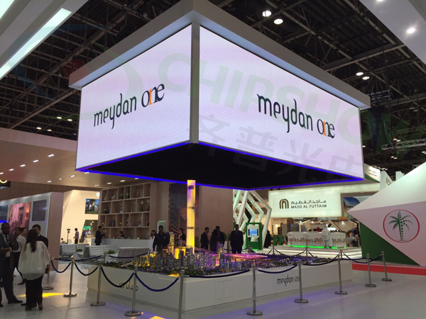 A suspended four-sided cube LED screen showing Meydan One logos above an architectural model.