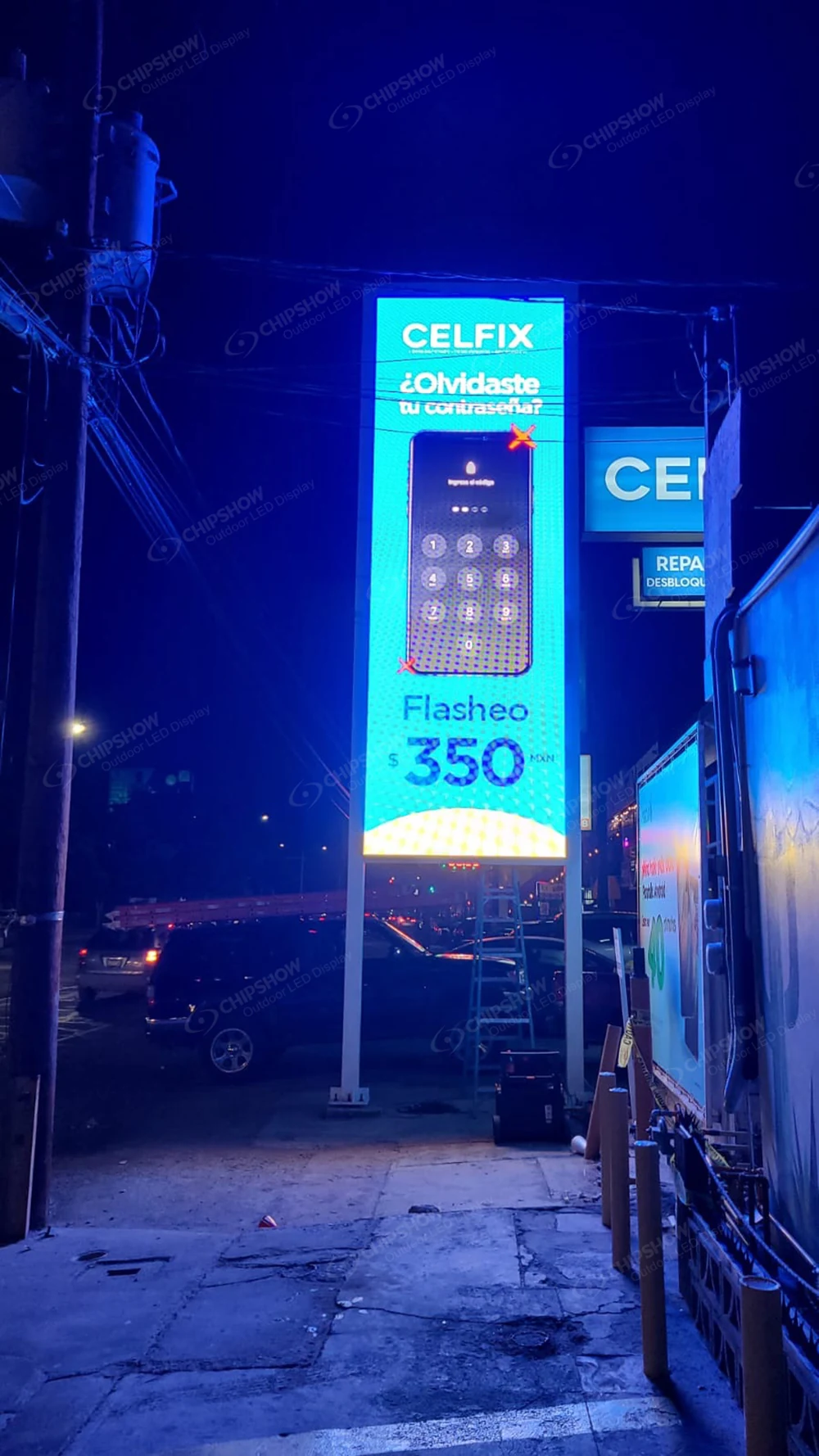 Vertical outdoor LED advertising screen at night displaying a mobile phone commercial