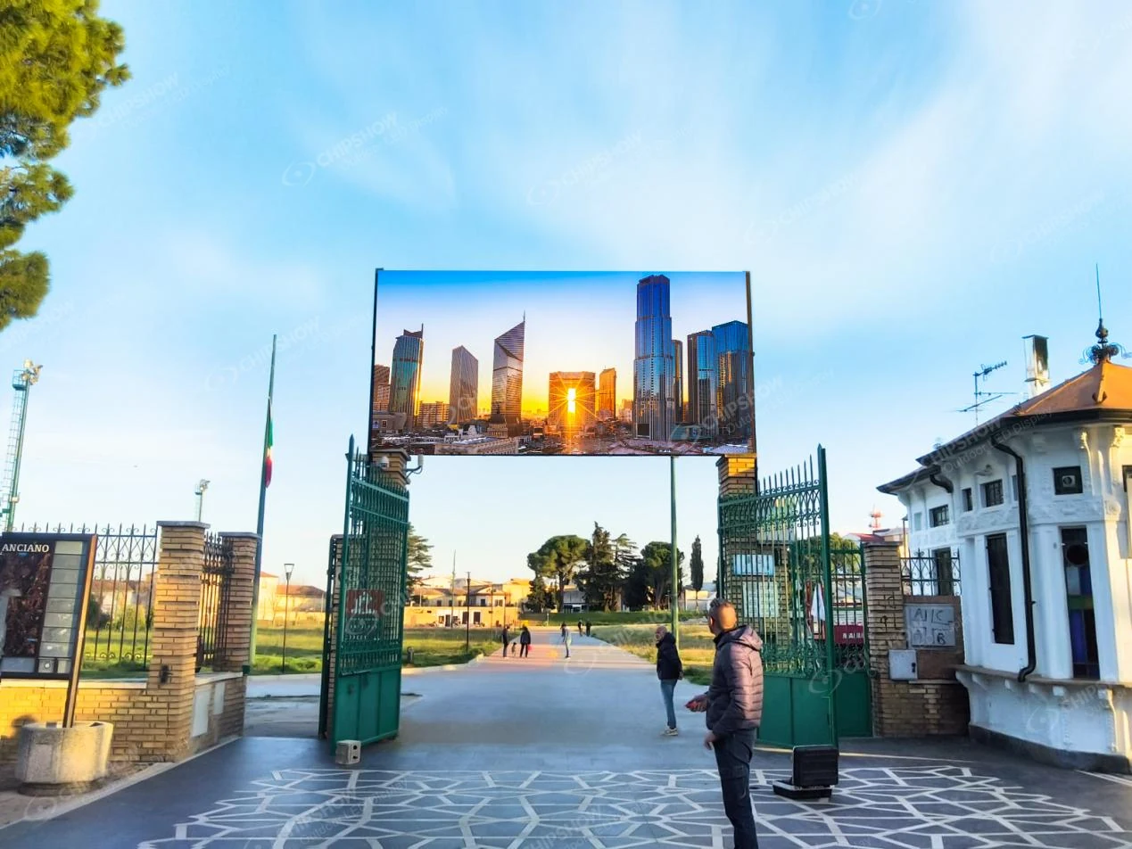 Outdoor LED billboard mounted above an entrance gate displaying a city skyline advertisement